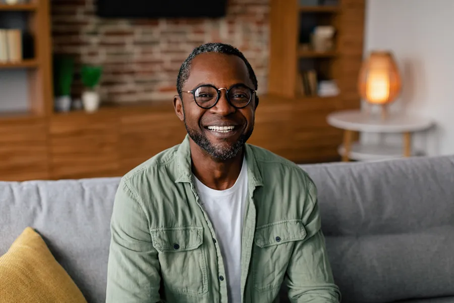 Andropause-Doctor A middle aged black man in a green button up shirt sits on his couch smiling, happy with his treatment for andropause and low testosterone from Fonthealth in Niagara.