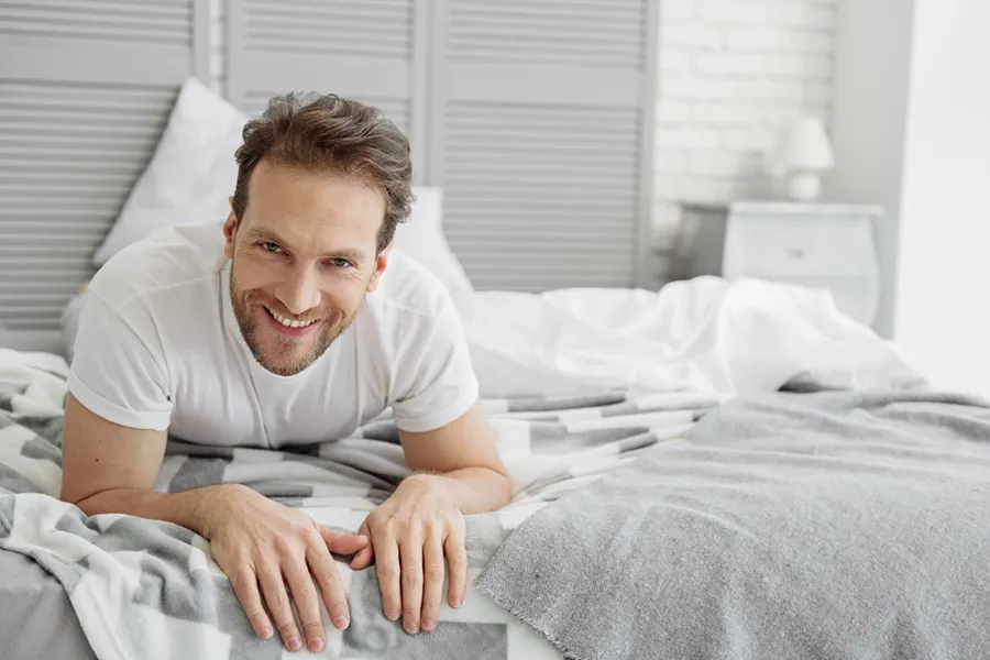 Low-Libido-in-Men-Doctor A dirty-blonde haired man lays on his stomach in bed smiling. Schedule treatment for low libido in men from Fonthealth in Niagara.