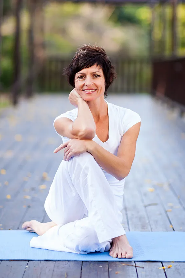 Niagara-Menopause-Treatment Confident middle-aged woman sitting on a yoga mat outdoors, smiling and relaxed after visiting Fonthealth in Niagara for menopause symptom treatment.