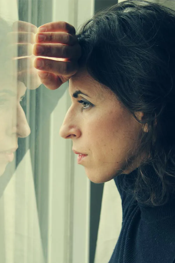 PCOS-Treatment A brunette woman in a thin dark turtleneck looks out the window with a serious expression, suffering from PCOS. Get treatment for Polycistic Ovarian Syndrome/PCOS from Fonthealth in Niagara.