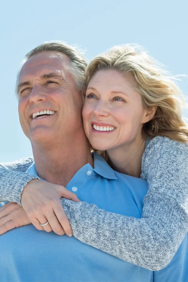 TMJ-Relief-Treatment A mature couple with big smiles embrace looking up into the sunny sky. Get TMJ relief treatment from Fonthealth in Niagara.