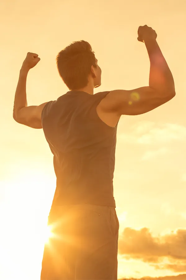 A motivational image of a young man standing with his back to the camera, arms raised triumphantly against a sunrise. Representing Wegovy Weight Loss Injections offered by Fonthealth in Niagara.