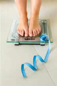 Weight-Loss-Resistance-Treatment Close-up of a woman's feet standing on a scale, with measuring tape by her toes, getting treatment for weight loss resistance from Fonthealth in Niagara.