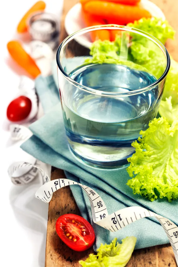 A vibrant still life of healthy eating and fitness. It features a glass of water, fresh vegetables like tomatoes and carrots, a tape measure, and fitness equipment. Representing Zepbound Weight Loss Injections offered by Fonthealth in Niagara.